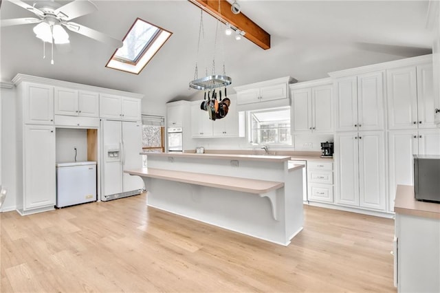 kitchen featuring white appliances, pendant lighting, a center island, lofted ceiling with skylight, and white cabinetry