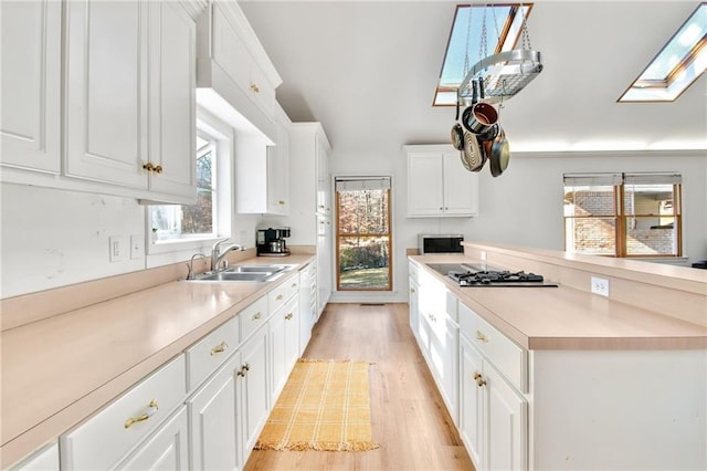 kitchen featuring light hardwood / wood-style floors, stainless steel gas stovetop, a skylight, white cabinets, and sink