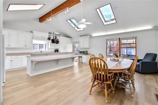 dining room with a healthy amount of sunlight, a skylight, track lighting, and beamed ceiling