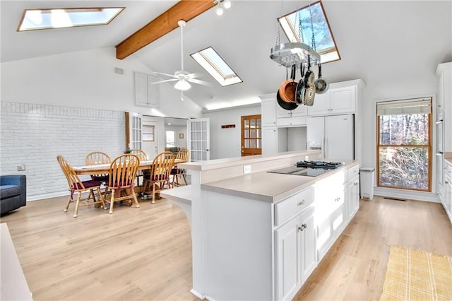 kitchen featuring white refrigerator with ice dispenser, lofted ceiling with skylight, a kitchen island, white cabinetry, and black stovetop