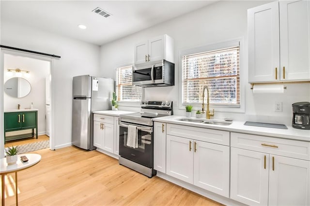 kitchen with stainless steel appliances, white cabinetry, light hardwood / wood-style floors, and sink