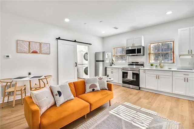 kitchen featuring stacked washer / drying machine, a barn door, white cabinetry, appliances with stainless steel finishes, and sink