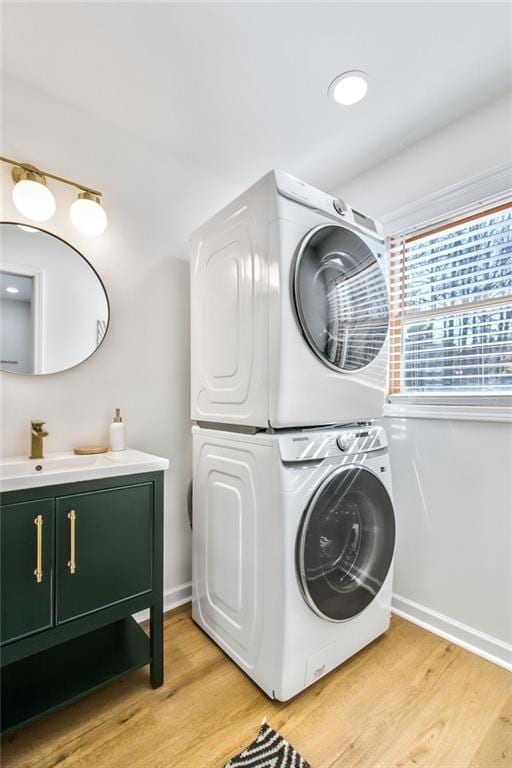 clothes washing area with sink, stacked washer and clothes dryer, cabinets, and light hardwood / wood-style flooring