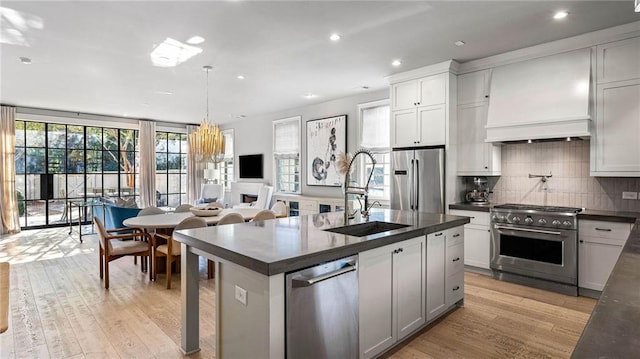 kitchen with an island with sink, stainless steel appliances, sink, decorative light fixtures, and light hardwood / wood-style floors