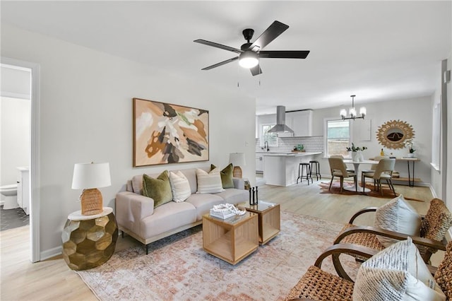 living room with sink, ceiling fan with notable chandelier, and light wood-type flooring