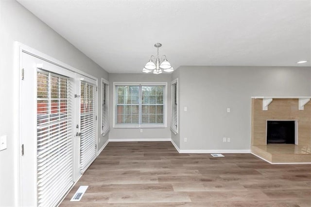 unfurnished dining area with a tiled fireplace, hardwood / wood-style floors, and a notable chandelier