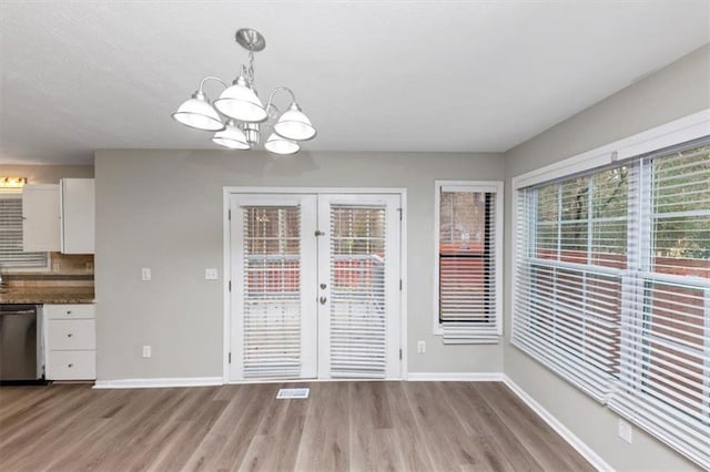 unfurnished dining area with an inviting chandelier, light hardwood / wood-style floors, and french doors