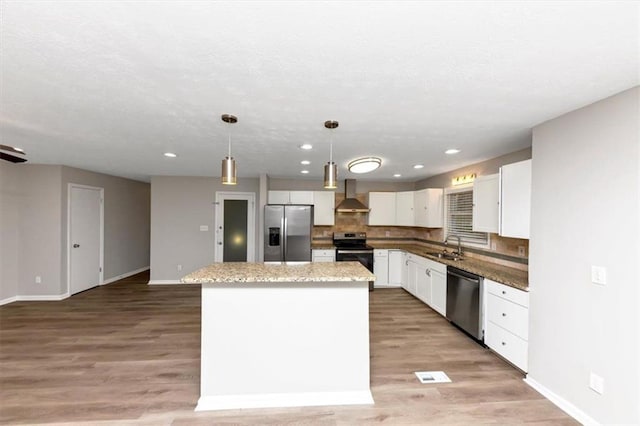 kitchen featuring a kitchen island, pendant lighting, white cabinets, stainless steel appliances, and wall chimney range hood