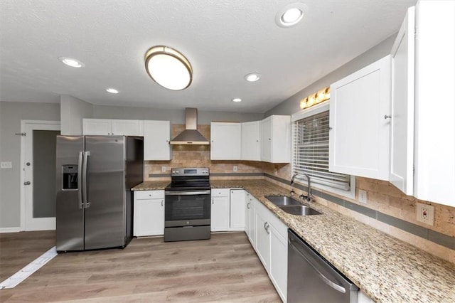 kitchen with white cabinets, appliances with stainless steel finishes, sink, and wall chimney range hood