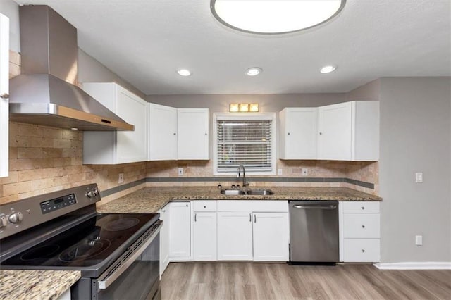 kitchen featuring appliances with stainless steel finishes, white cabinetry, sink, dark stone countertops, and wall chimney range hood