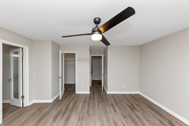 unfurnished bedroom featuring ceiling fan, a walk in closet, a textured ceiling, and light wood-type flooring