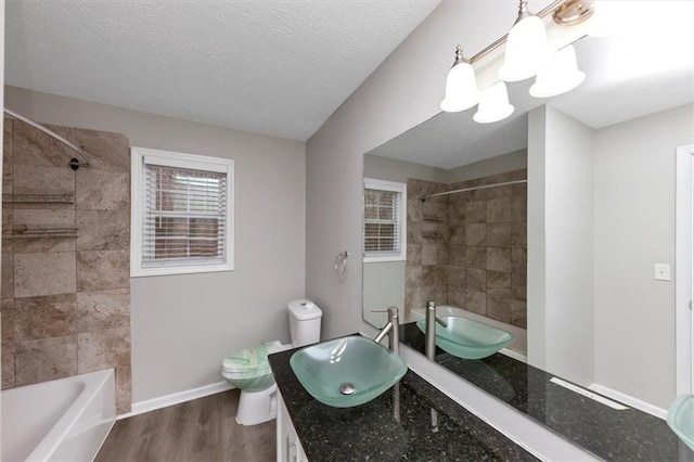 full bathroom featuring hardwood / wood-style flooring, vanity, a textured ceiling, toilet, and tiled shower / bath