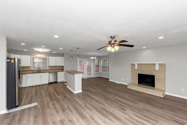 kitchen with appliances with stainless steel finishes, wood-type flooring, white cabinets, hanging light fixtures, and a center island