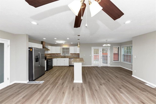 kitchen with pendant lighting, white cabinetry, sink, stainless steel appliances, and wall chimney range hood