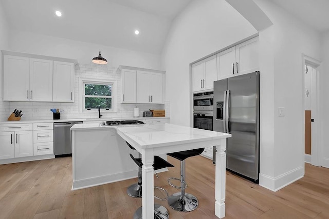 kitchen with white cabinetry, light stone counters, a center island, light hardwood / wood-style flooring, and appliances with stainless steel finishes