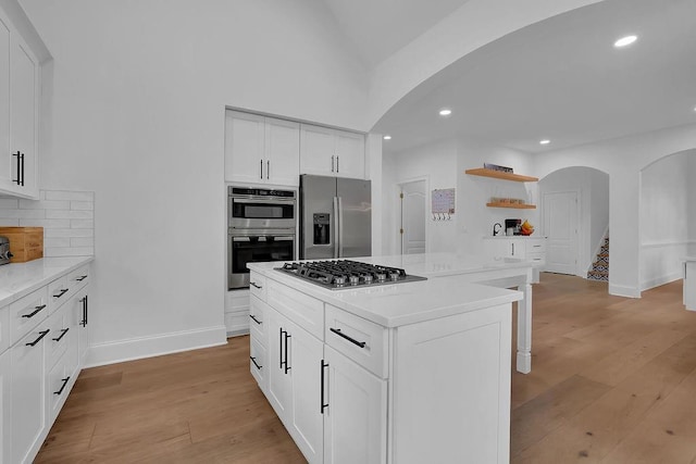 kitchen with light hardwood / wood-style flooring, appliances with stainless steel finishes, backsplash, a center island, and white cabinets