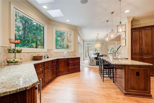 kitchen featuring a kitchen breakfast bar, decorative light fixtures, a wealth of natural light, light stone counters, and a skylight