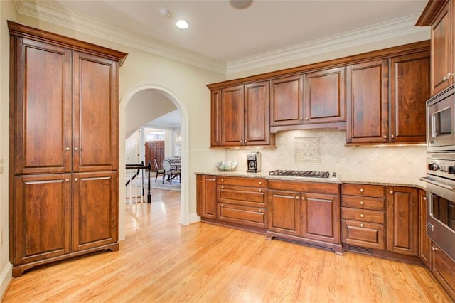 kitchen with light wood-type flooring, stainless steel appliances, light stone counters, and decorative backsplash