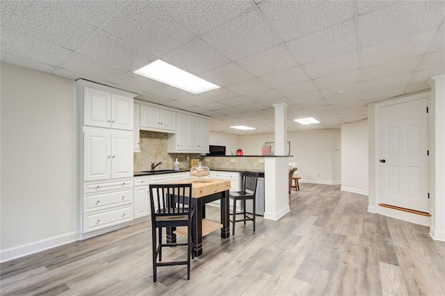 kitchen featuring a kitchen bar, tasteful backsplash, white cabinetry, sink, and light wood-type flooring