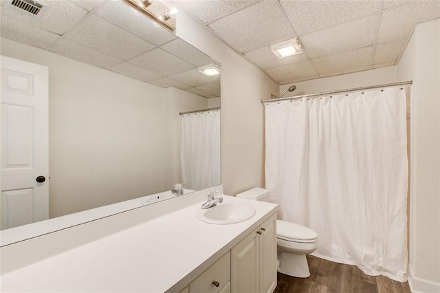 bathroom with wood-type flooring, toilet, a drop ceiling, and vanity