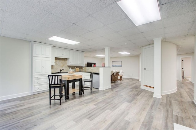 kitchen featuring stainless steel dishwasher, a paneled ceiling, white cabinetry, tasteful backsplash, and a breakfast bar area