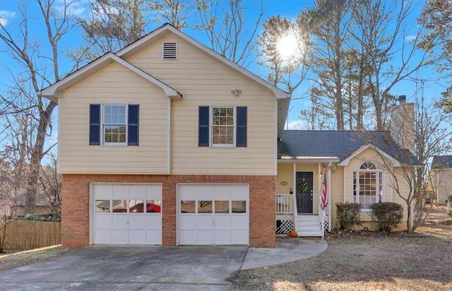 tri-level home with brick siding, a chimney, a porch, concrete driveway, and a garage