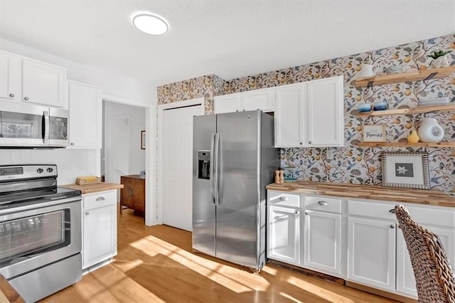 kitchen with stainless steel appliances, wood counters, white cabinets, and wallpapered walls