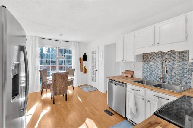 kitchen featuring butcher block countertops, a sink, white cabinets, light wood-style floors, and appliances with stainless steel finishes