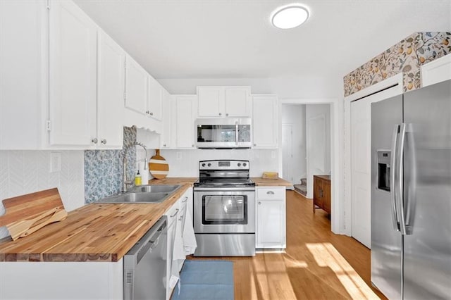 kitchen with white cabinets, butcher block counters, appliances with stainless steel finishes, light wood-type flooring, and a sink