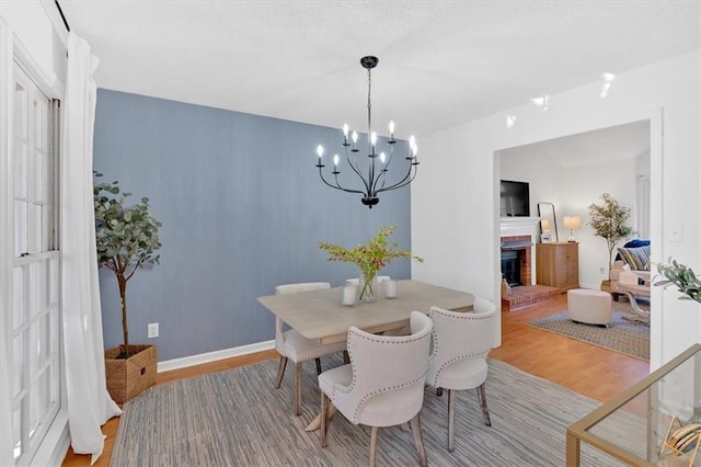 dining room with a notable chandelier, a fireplace, a textured ceiling, wood finished floors, and baseboards