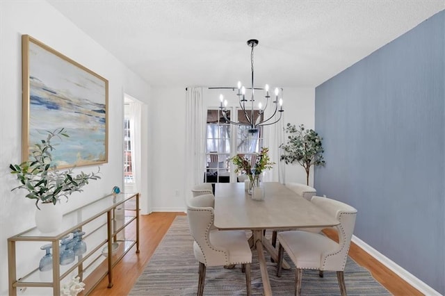 dining area featuring light wood-style flooring, baseboards, a chandelier, and a textured ceiling