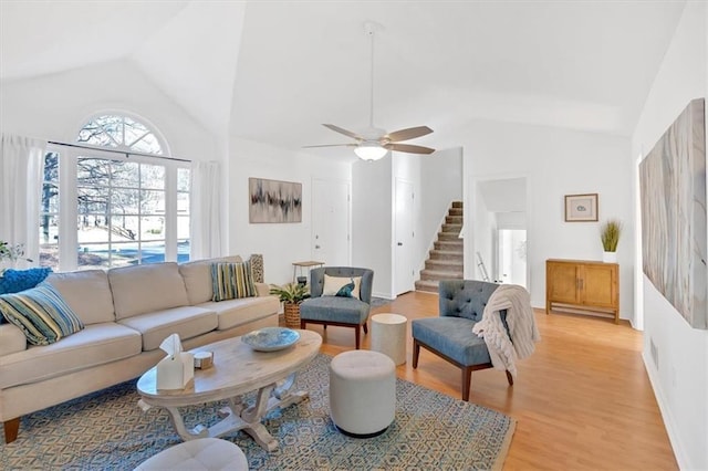 living area featuring baseboards, a ceiling fan, stairs, vaulted ceiling, and light wood-type flooring