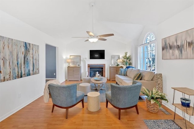 living area featuring a brick fireplace, a ceiling fan, vaulted ceiling, and wood finished floors