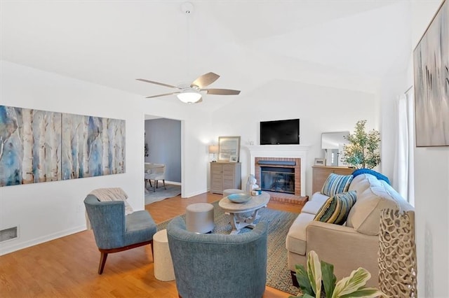 living room featuring baseboards, ceiling fan, vaulted ceiling, light wood-type flooring, and a brick fireplace