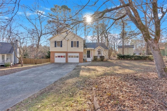 tri-level home with driveway, a chimney, an attached garage, fence, and brick siding