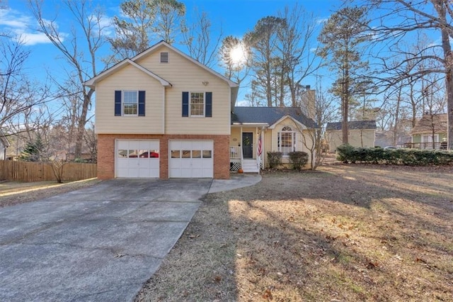 tri-level home featuring driveway, a garage, a chimney, fence, and brick siding