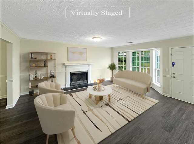 living area with a fireplace with raised hearth, ornamental molding, a textured ceiling, wood finished floors, and baseboards