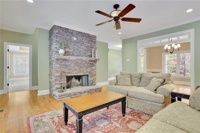 living room featuring crown molding, light hardwood / wood-style flooring, a fireplace, and ceiling fan with notable chandelier