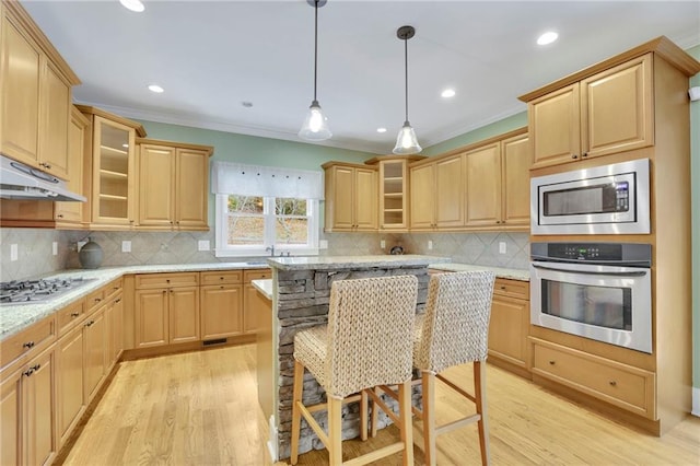 kitchen with crown molding, appliances with stainless steel finishes, a kitchen bar, light hardwood / wood-style floors, and light stone counters