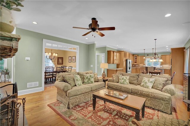 living room featuring crown molding, ceiling fan with notable chandelier, and light wood-type flooring