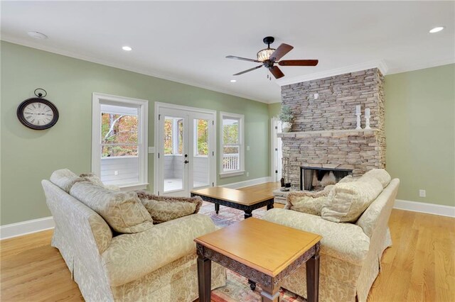 living room featuring french doors, a stone fireplace, light hardwood / wood-style floors, ceiling fan, and crown molding