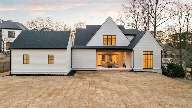 back of property at dusk with roof with shingles and a patio area