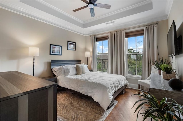 bedroom with crown molding, ceiling fan, wood-type flooring, and a raised ceiling