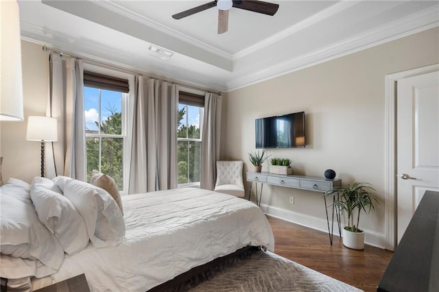 bedroom with ornamental molding, dark wood-type flooring, ceiling fan, and a tray ceiling