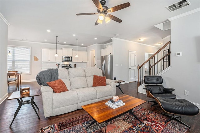 living room featuring dark wood-style flooring, visible vents, baseboards, stairs, and ornamental molding