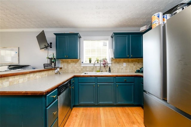 kitchen featuring a sink, tasteful backsplash, appliances with stainless steel finishes, a peninsula, and light wood finished floors