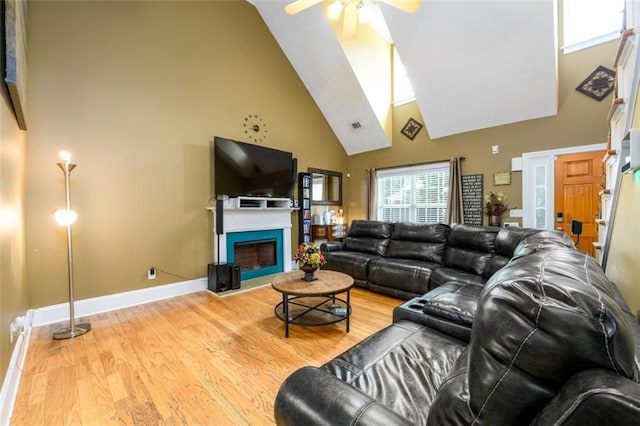 living area featuring high vaulted ceiling, a ceiling fan, light wood-style floors, a fireplace, and baseboards