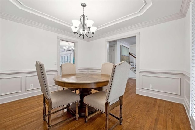 dining space with wood-type flooring, a tray ceiling, an inviting chandelier, and crown molding