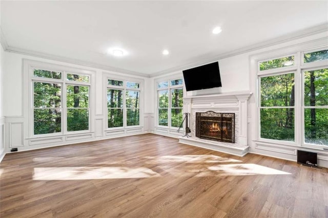 unfurnished living room featuring a premium fireplace, a healthy amount of sunlight, ornamental molding, and hardwood / wood-style flooring