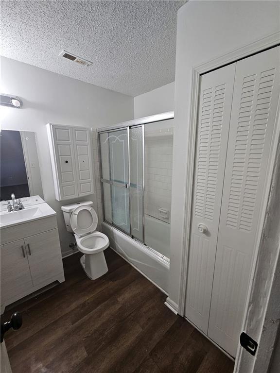 full bathroom featuring shower / bath combination with glass door, hardwood / wood-style flooring, vanity, toilet, and a textured ceiling